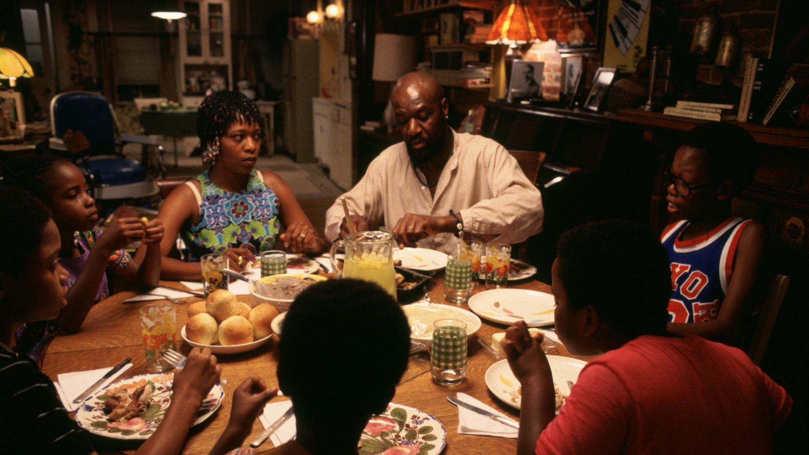 A family sits around a dinner table, with the parents in the back center of the frame