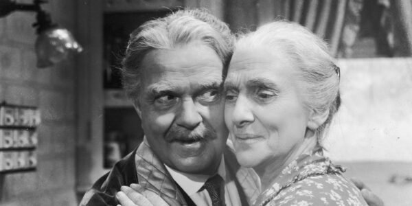 An elderly man and woman hold each other closely, their cheeks touching