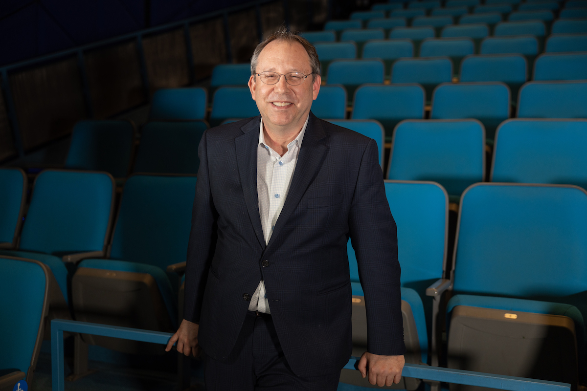 a man in a navy blazer stands in a theater with blue seats