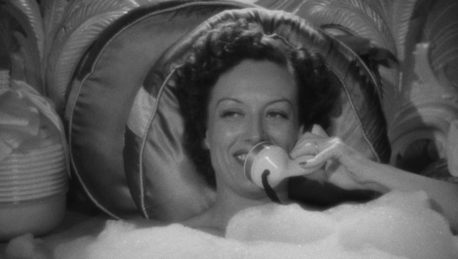 A smiling woman talks on the phone while taking a bubble bath
