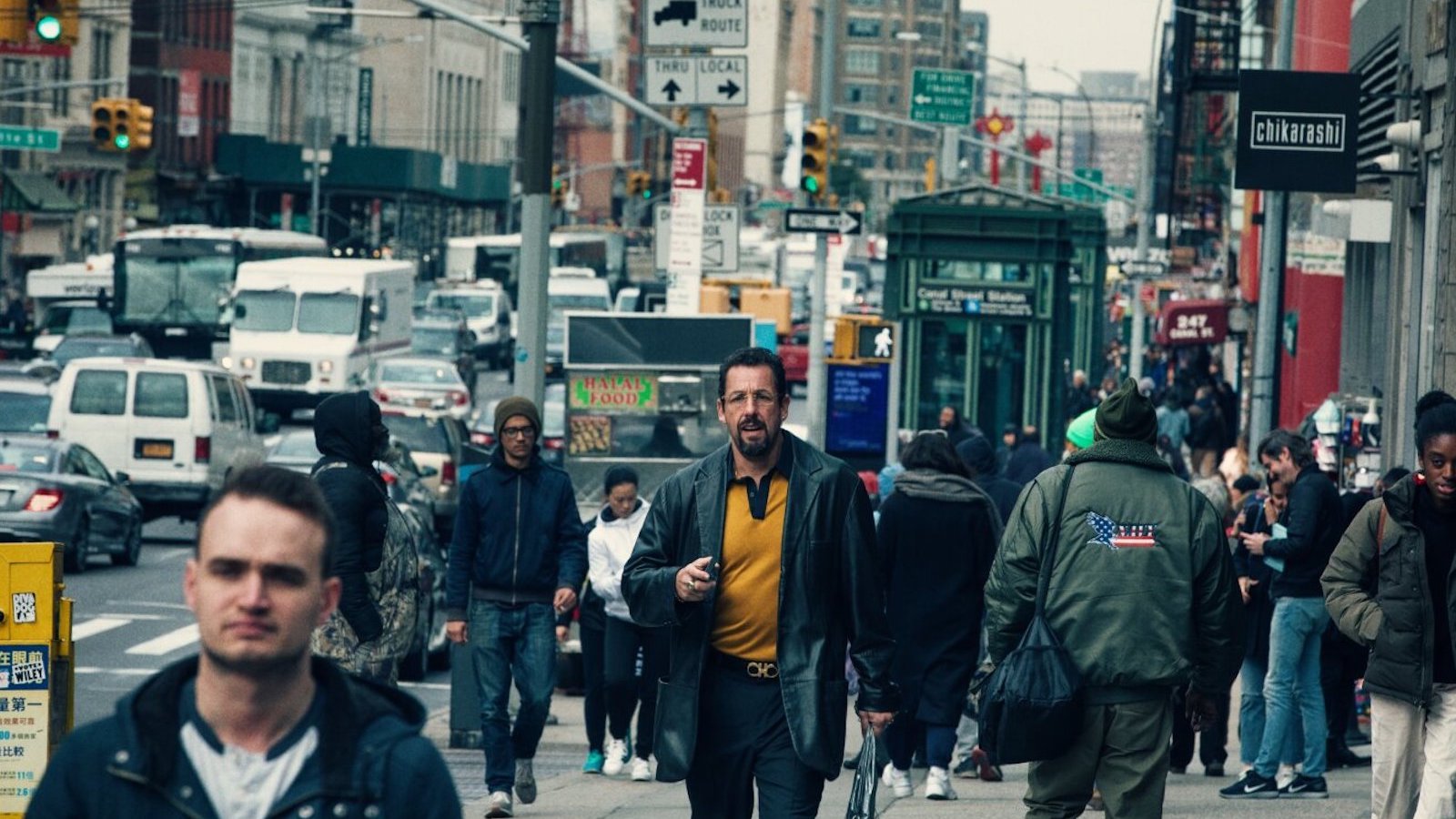 A man in yellow shirt and blue jacket walks through a crowded midtown NYC street
