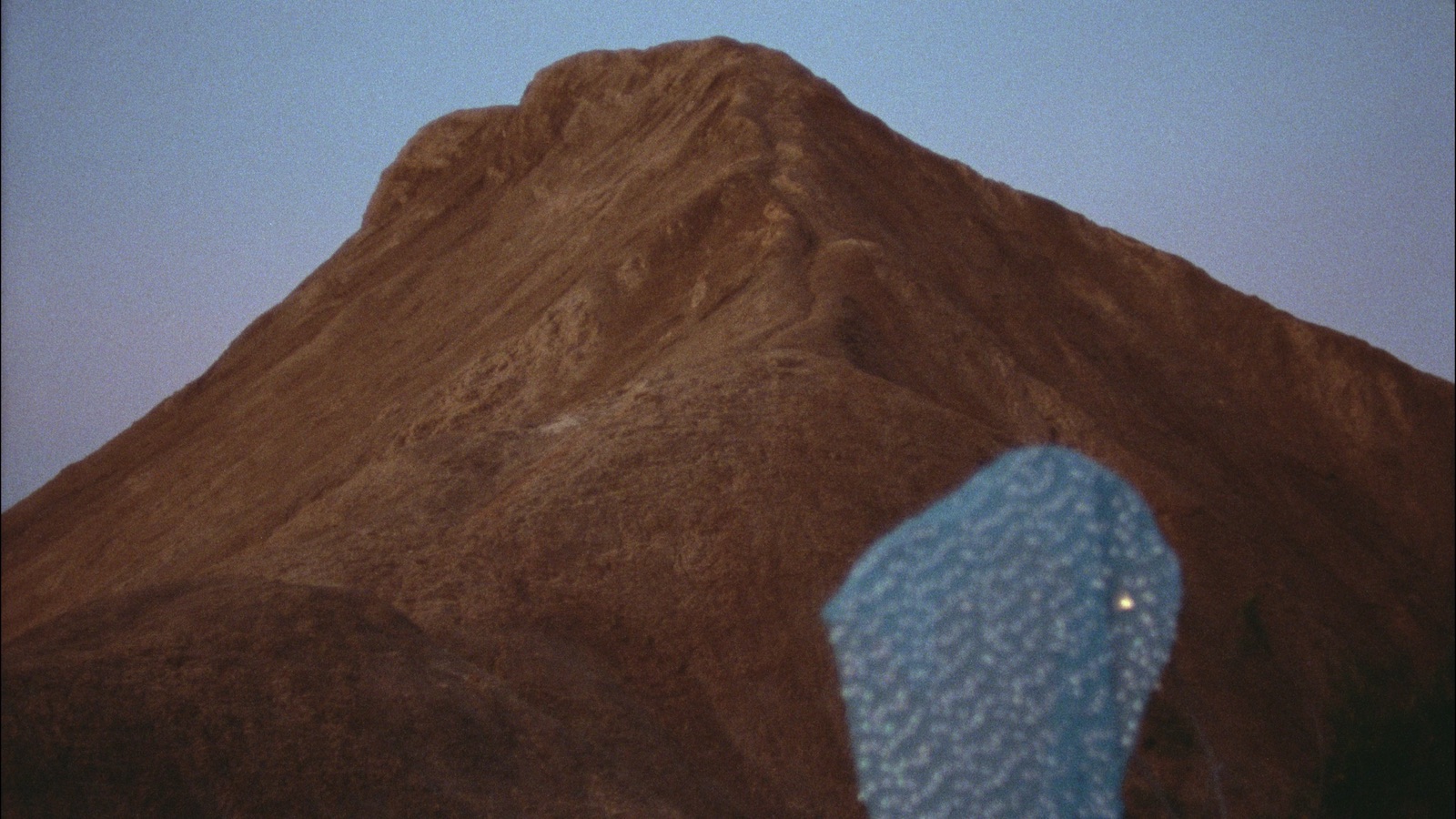 a mountain wth a blue shawled figure in the foreground