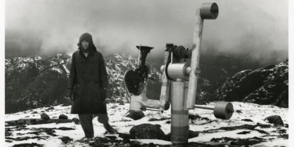 A man stands on a mountaintop next to an apparatus with a telescope