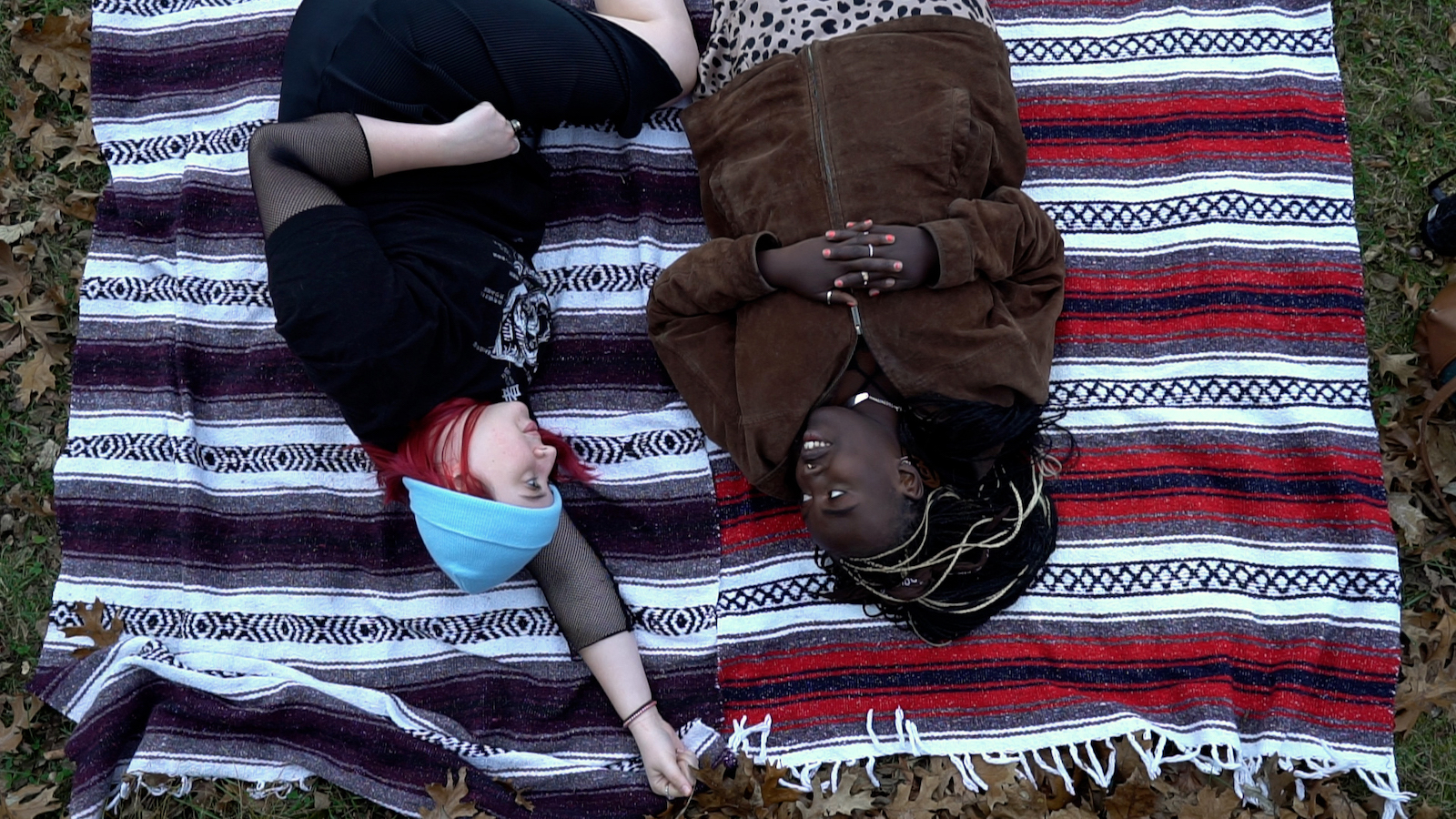 Two young women lie on a blanket outside talking to each other, the image is upside down