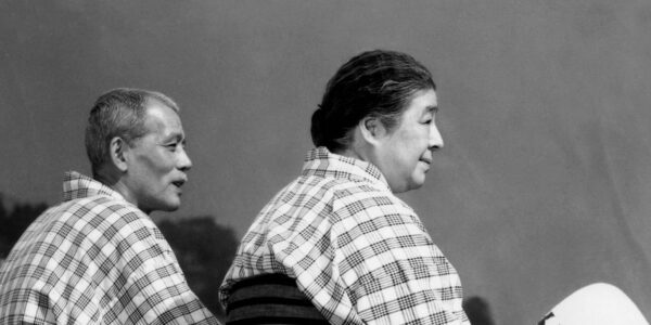 A man and a woman in kimonos sit in profile looking out at the sky