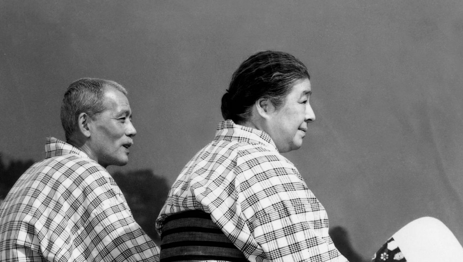 A man and a woman in kimonos sit in profile looking out at the sky