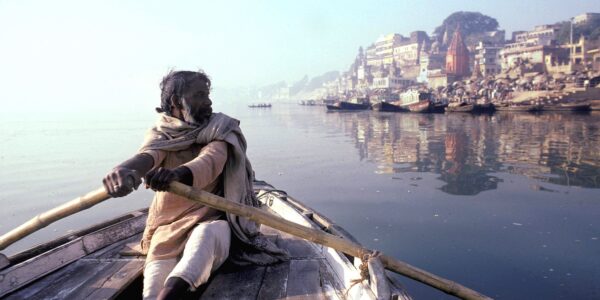 A man rows a boat towards a city on the river