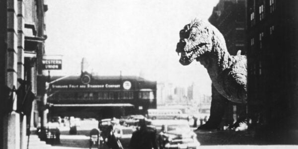 A black and white image of a gigantic dinosaur peeking out from the corner of a city street with people running in panic