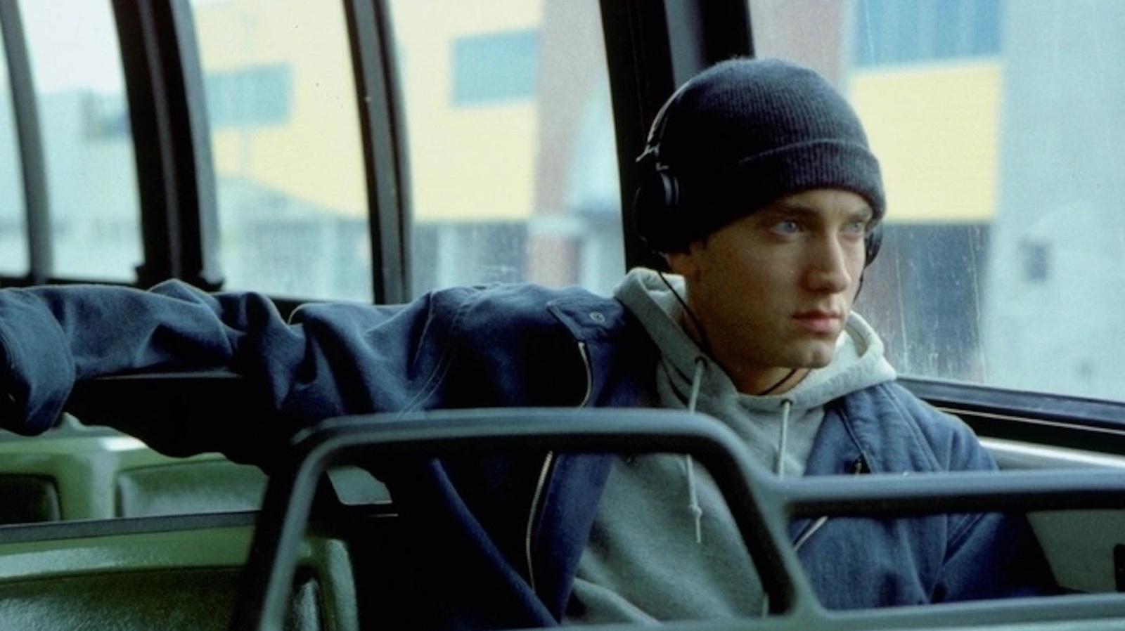 A man in a skull cap sits on a bus with headphones on looking out the window