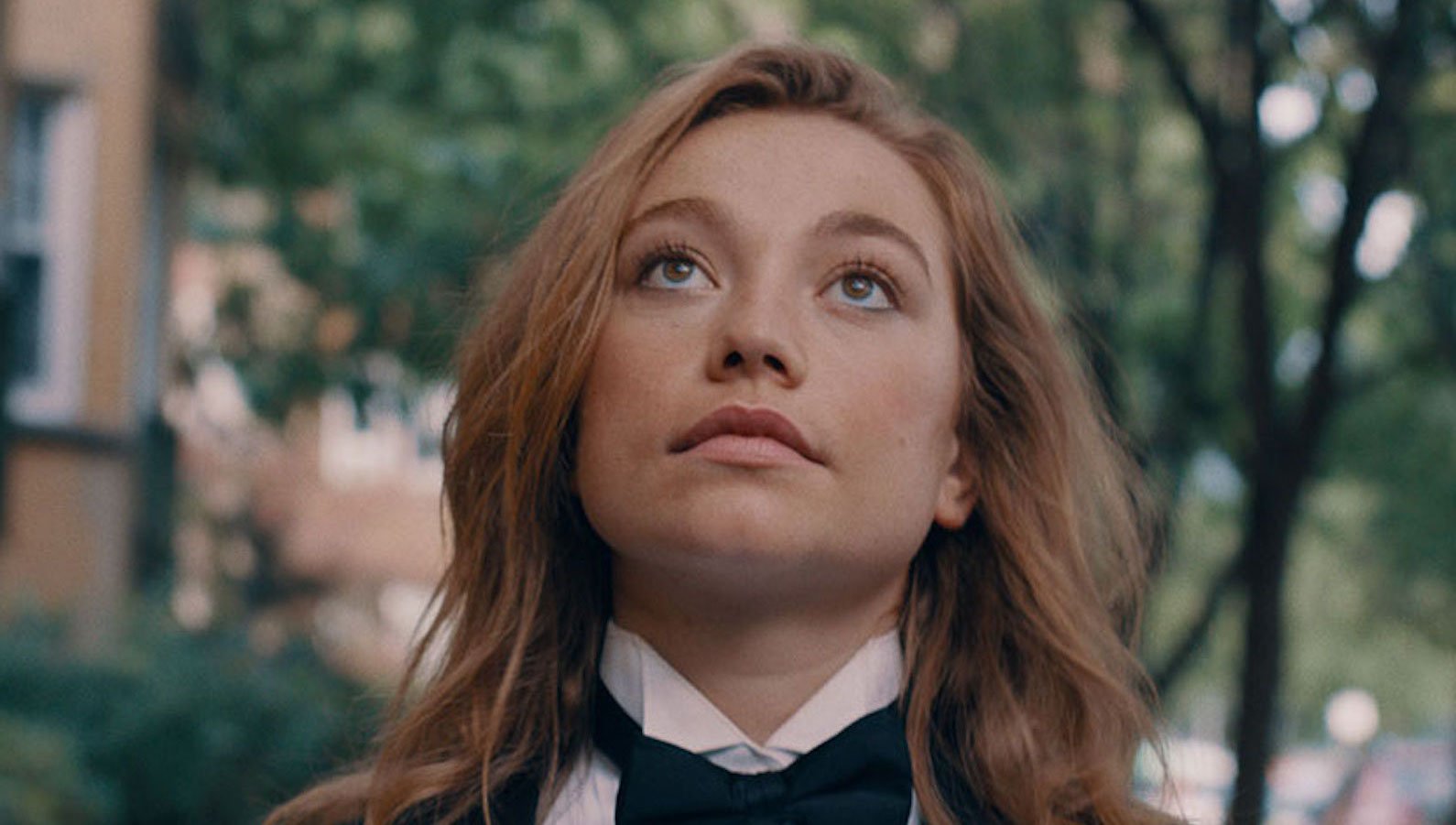 A girl with long red hair and wearing a tuxedo looks up