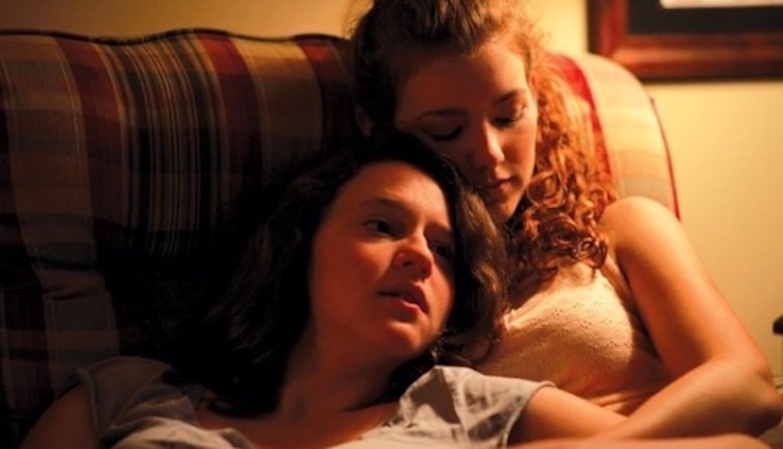 Two young woman sit on a couch, holding each other