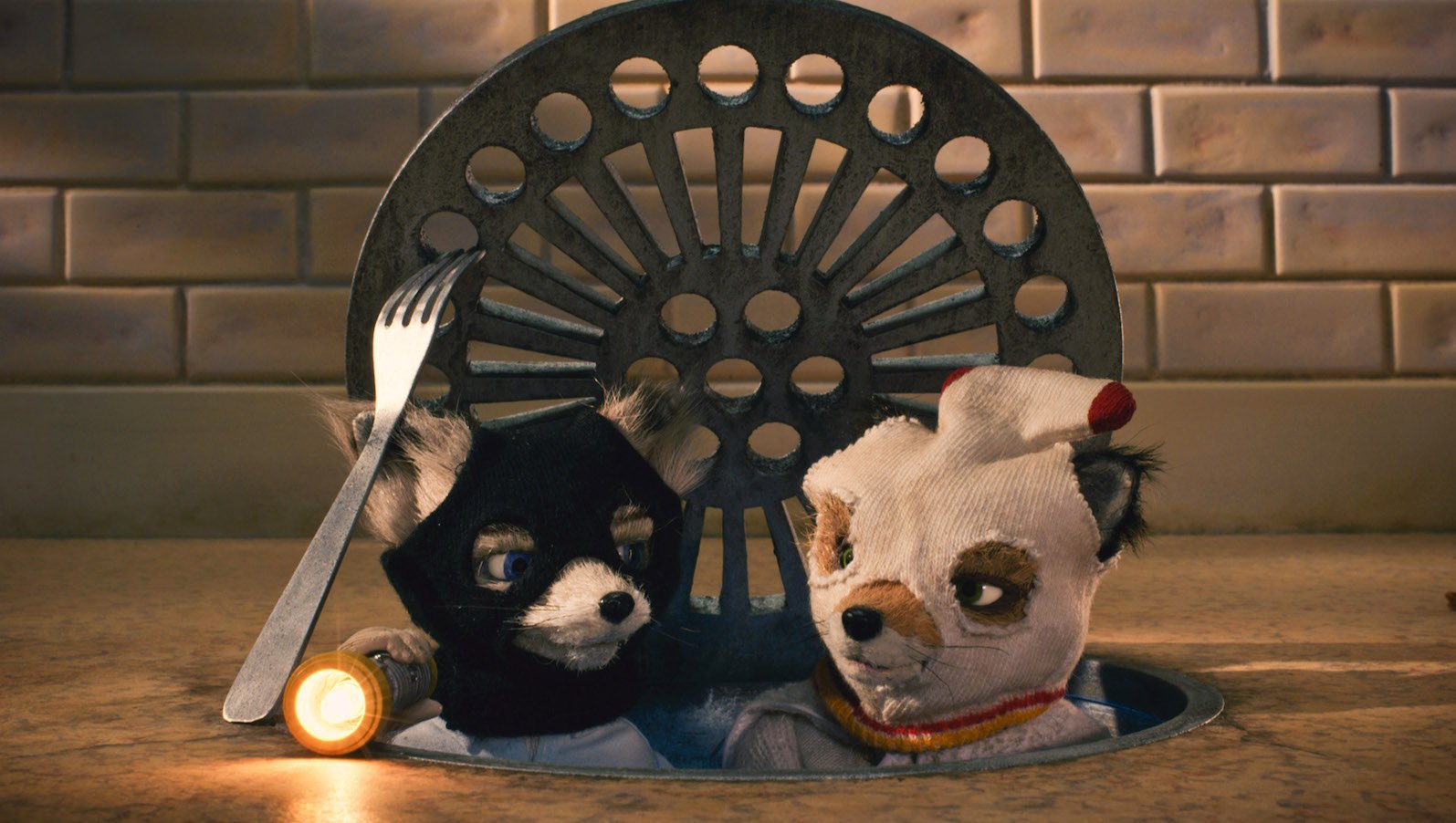 Two stop motion foxes with socks on their heads pop their heads out of a sewer manhole cover
