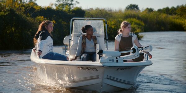 Three women sit in a motorboat moving up a river in the sunlight
