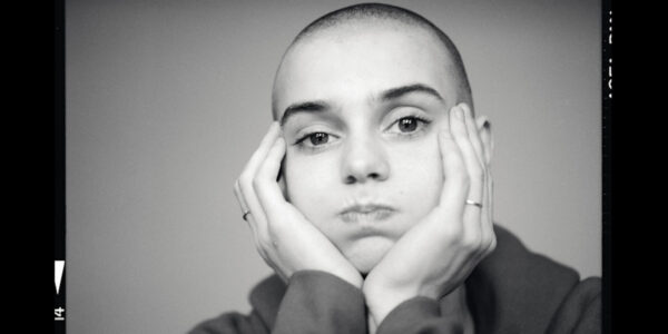 closeup on the face of a young white woman with a shaved head. Her hands frame her face.