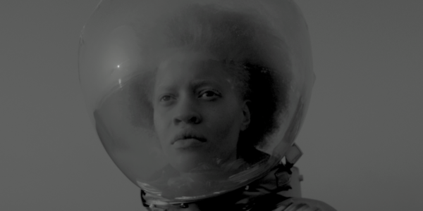 black and white image of a young black woman wearing a globe-like space helmet on her head