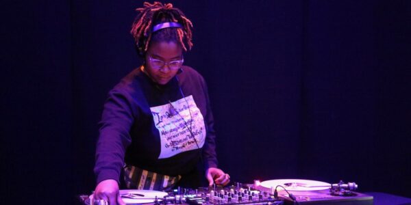 A black woman spins records at a DJ station