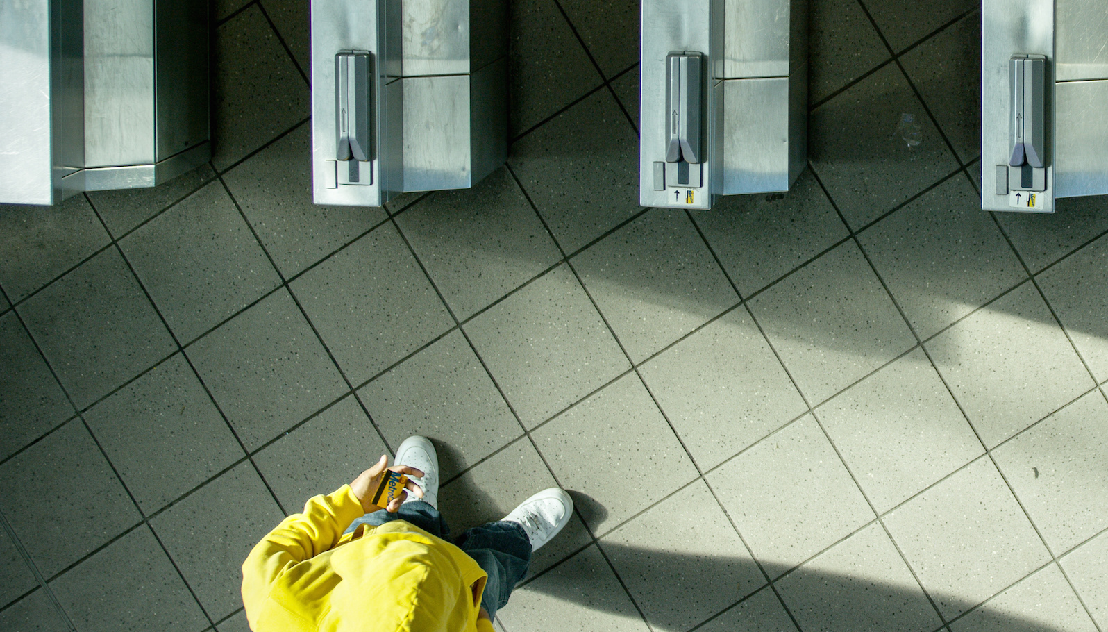 An overhead shot of a man in a yellow sweatshirt standing in front of subway turnstiles
