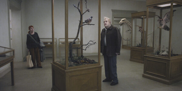A man with pale ghostly makeup stands looking at models of birds at a museum