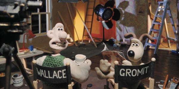 A claymation image of a man and his dog sitting on director's chairs, turning their heads back towards the camera